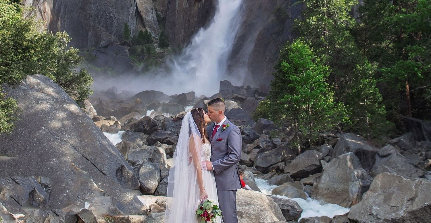 A couple posing for a wedding photoshoot in front of a waterfall in Yosemite - Narrow Gauge Inn - A Serenite Hotel Near Fish Camp.