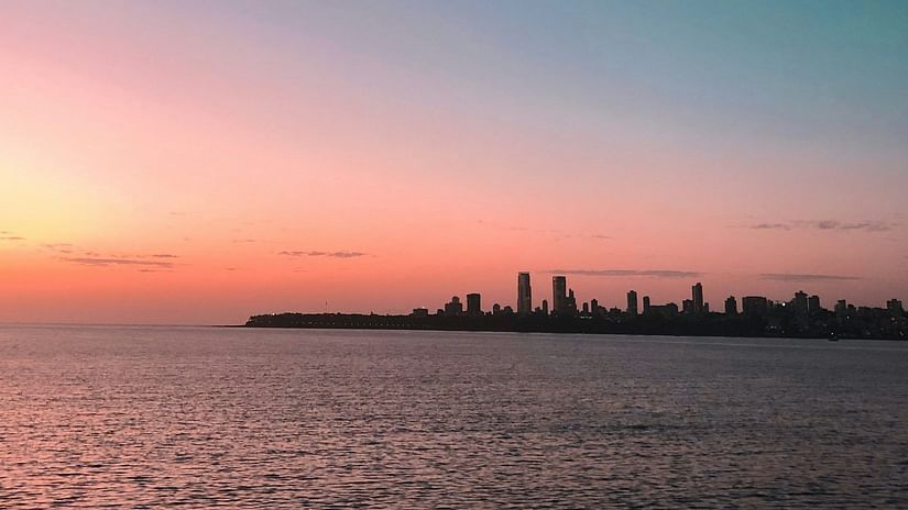 A pastel sunset over a calm sea with the silhouette of a city skyline in the distance