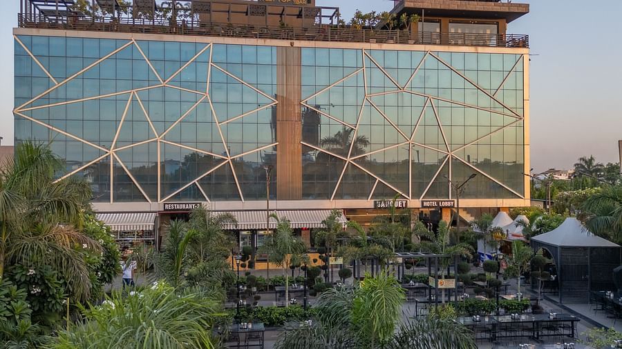 Vertical shot of the Hotel Highway King, Jaipur's glass exterior with red signage on top and garden spaces in front.