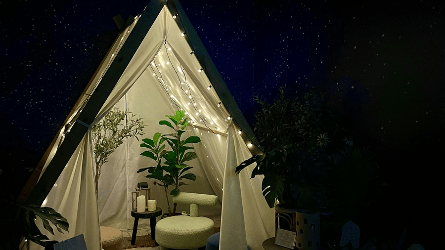 An outdoor view of a glamping tent at night, with a small table and chair set up on a porch in front.