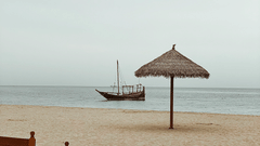 An overview of a beach in Qatar with a handmade canopy on the beach and a boat in the ocean.