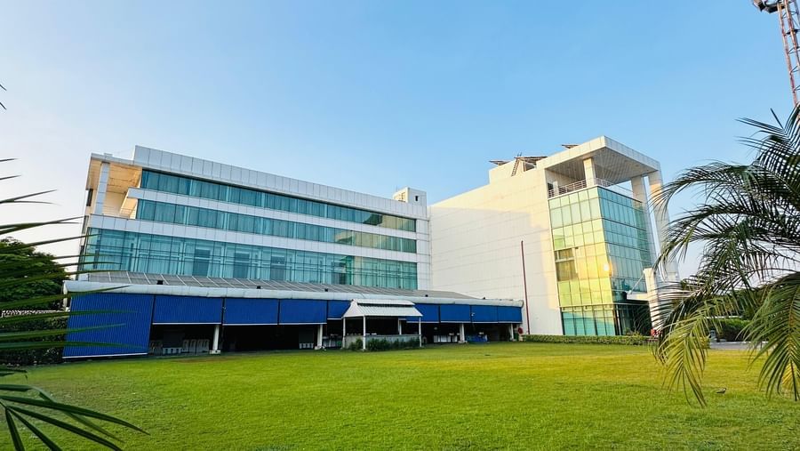  An exterior, wide-angle view of the modern Amer Greens hotel building, featuring multiple stories and a large, manicured green lawn in the foreground under a clear sky.