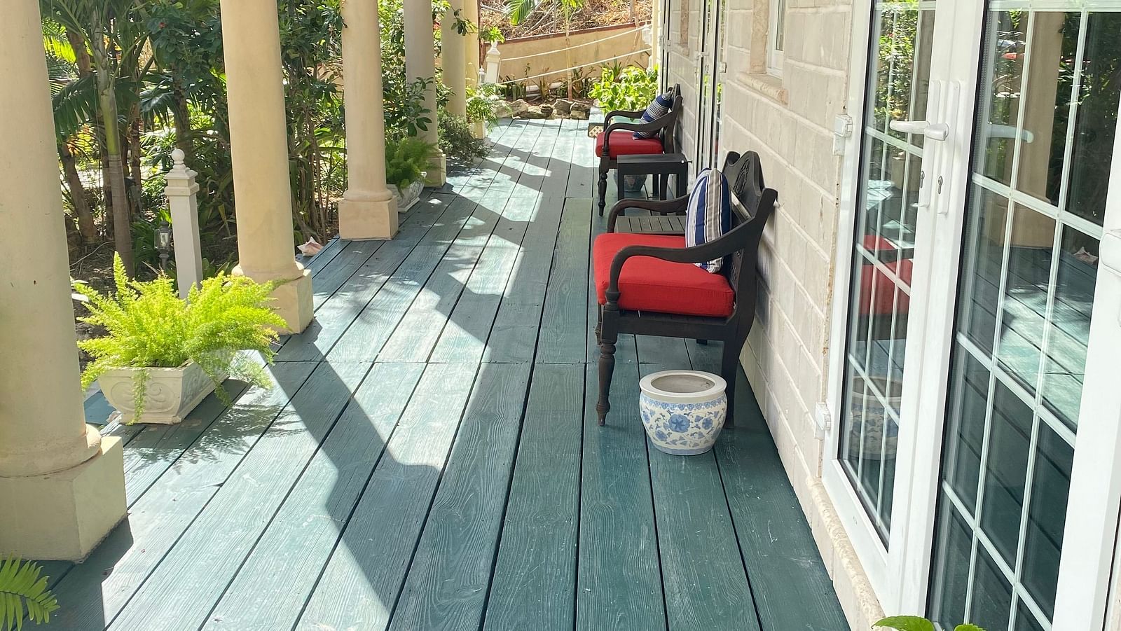 Outdoor walkway with green wooden flooring and red chairs outside a room | A Stone's Throw Away