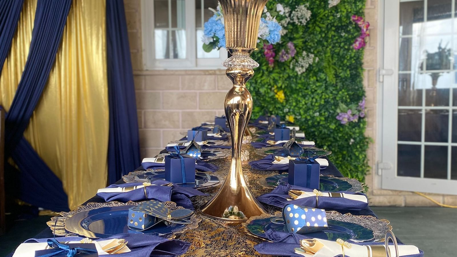 Long banquet table with navy blue napkins, golden cutlery, and tall floral centerpiece | A Stone's Throw Away