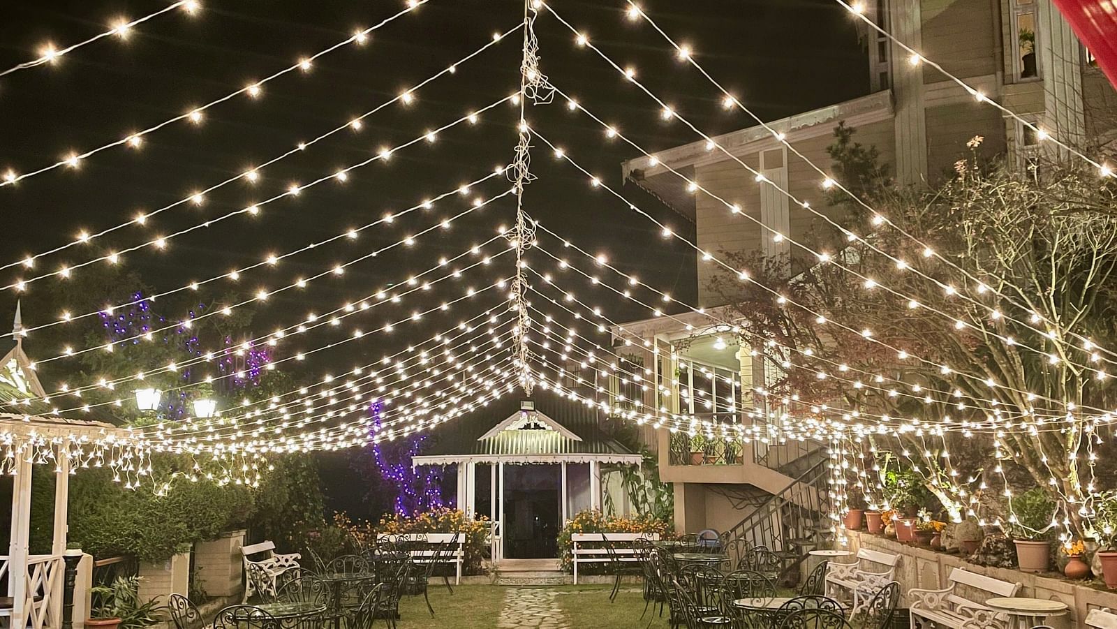 Evening wedding event at Cedar Inn, Darjeeling, showing festoon lights over the garden walkway and decorated seating area.