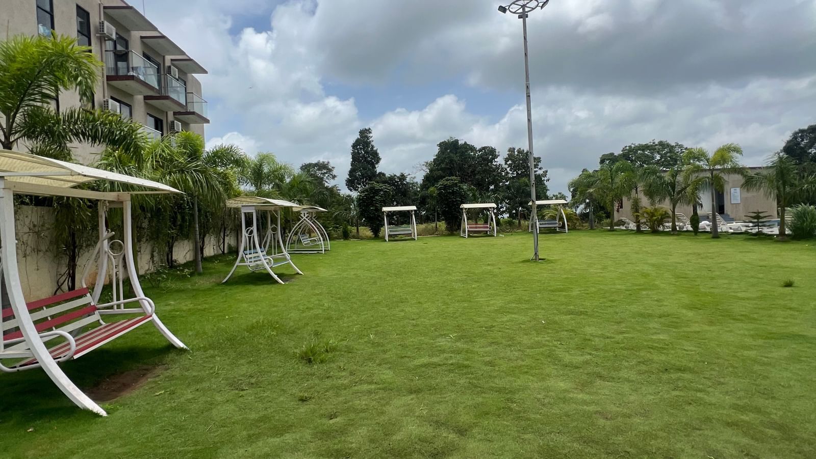Lawn area with multi-seating swings of Daksh The Valley Resort, Saputara, as seen under a cloudy sky.