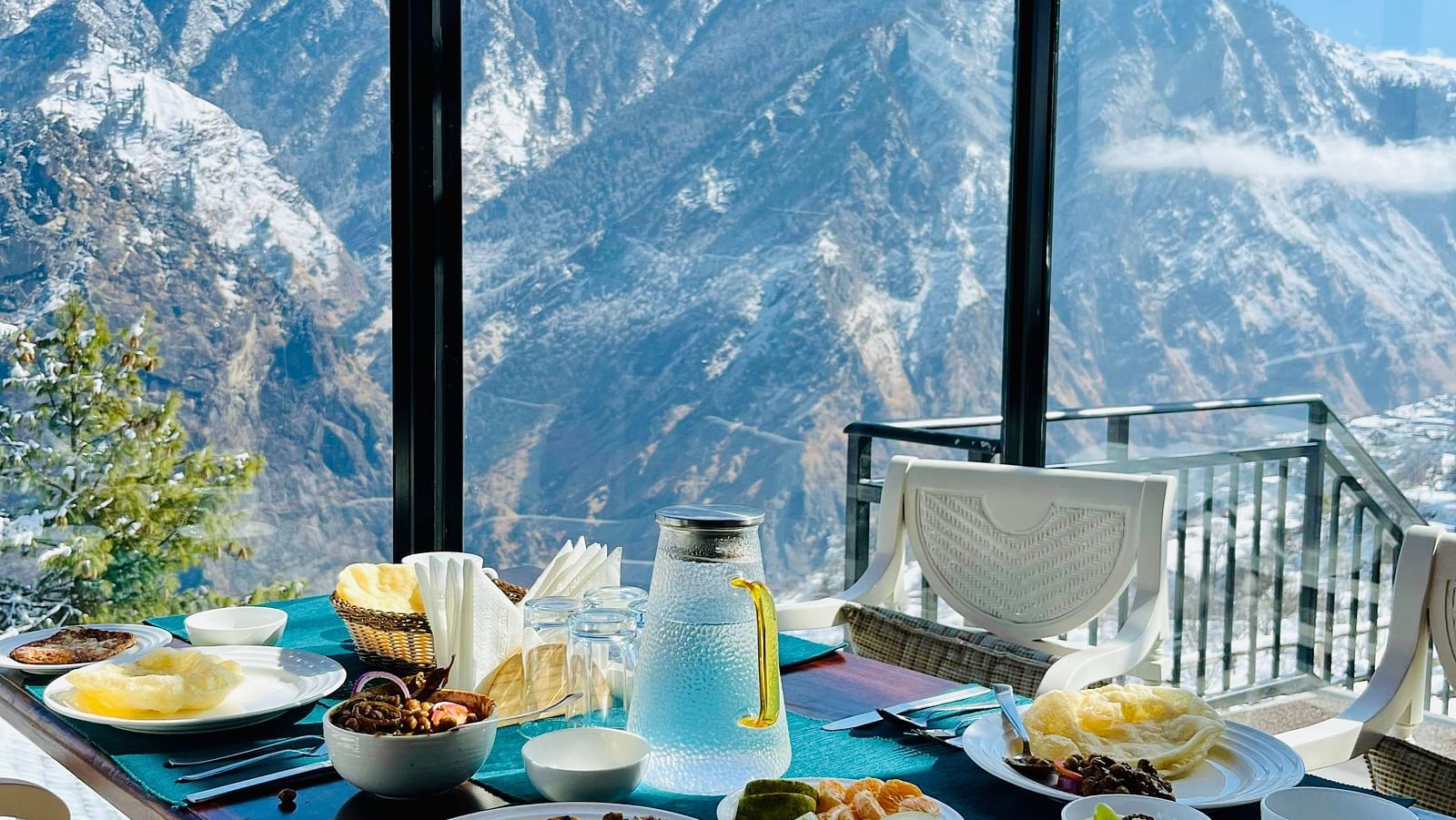 Image of dining table with a variety of food on the table and view of the mountains | Faraway Cottages, Auli