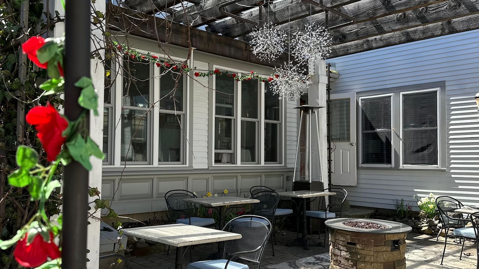 Covered patio with lattice roof, outdoor dining set, and hanging red flowers, attached to a white building.