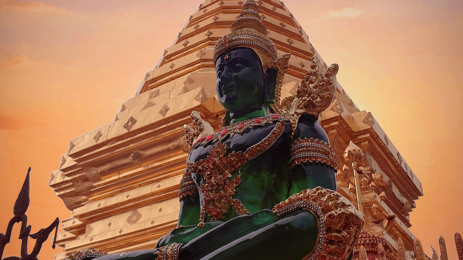An emerald buddha s statue in front of a temple after sunset with different hues in the sky.