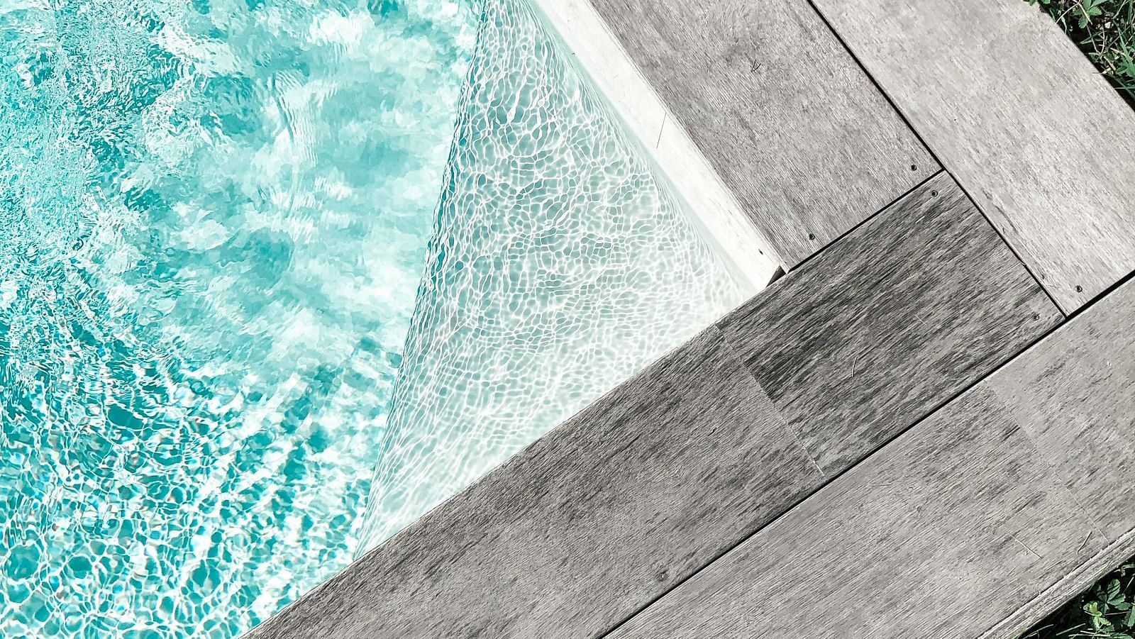 A close-up of a section of a swimming pool with clear blue water and wooden border..
