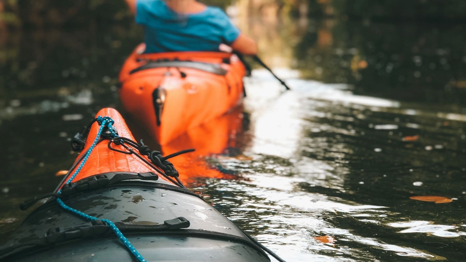 The bow of a canoe is visible in the foreground as  a woman paddles away in her canoe in front of it - kayaking in Kumarakom