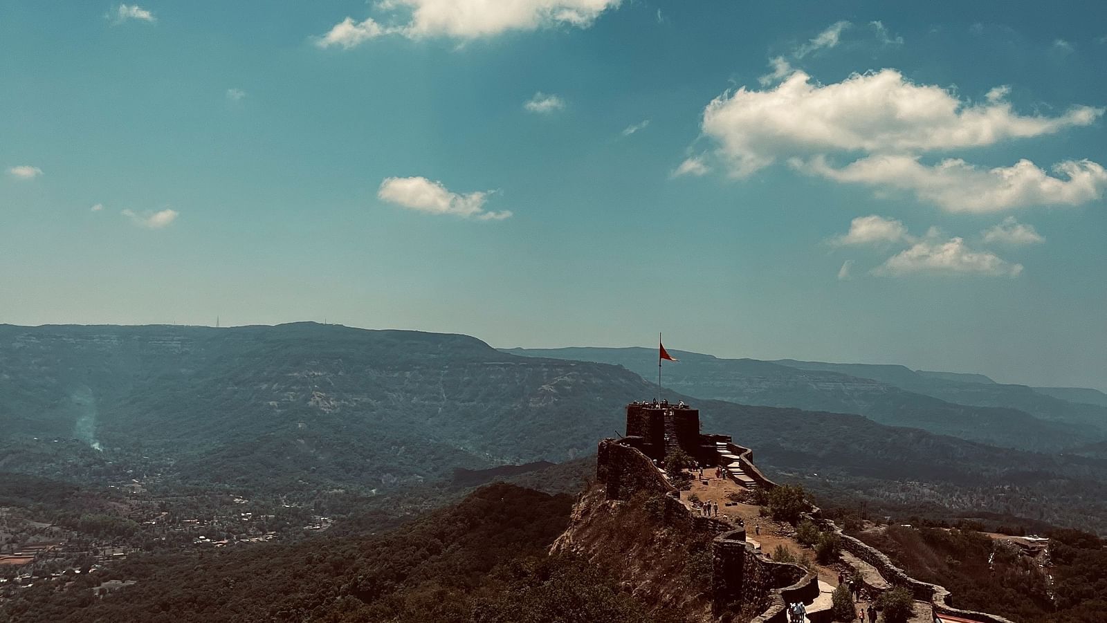 an image of a fort amidst hills with white clouds on blue sky 