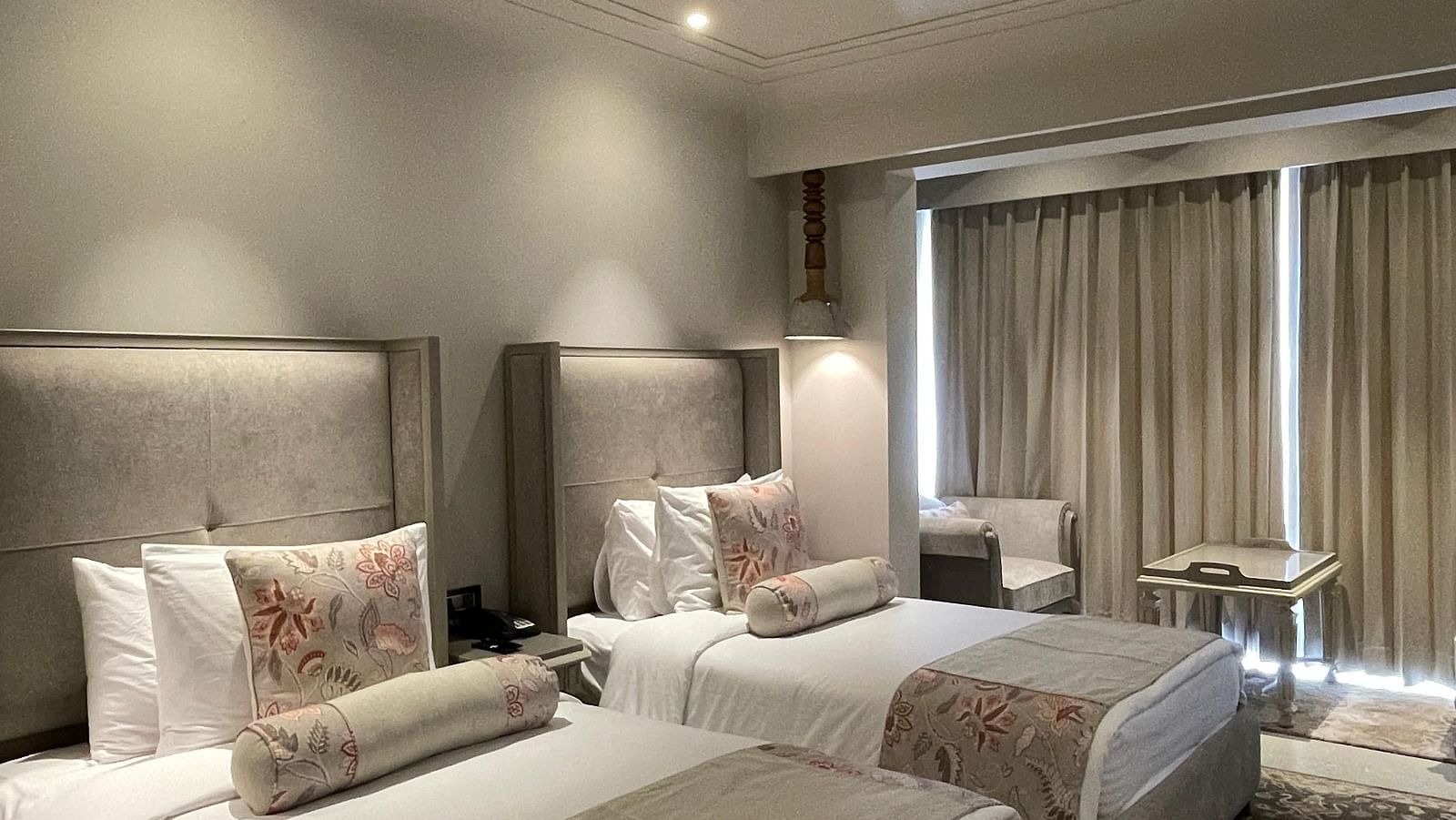 A spacious Premium Twin Room at The Evren, Vagator, with two single beds, each with a plush headboard and decorative pillows. The room features a patterned rug and a seating area near the window.