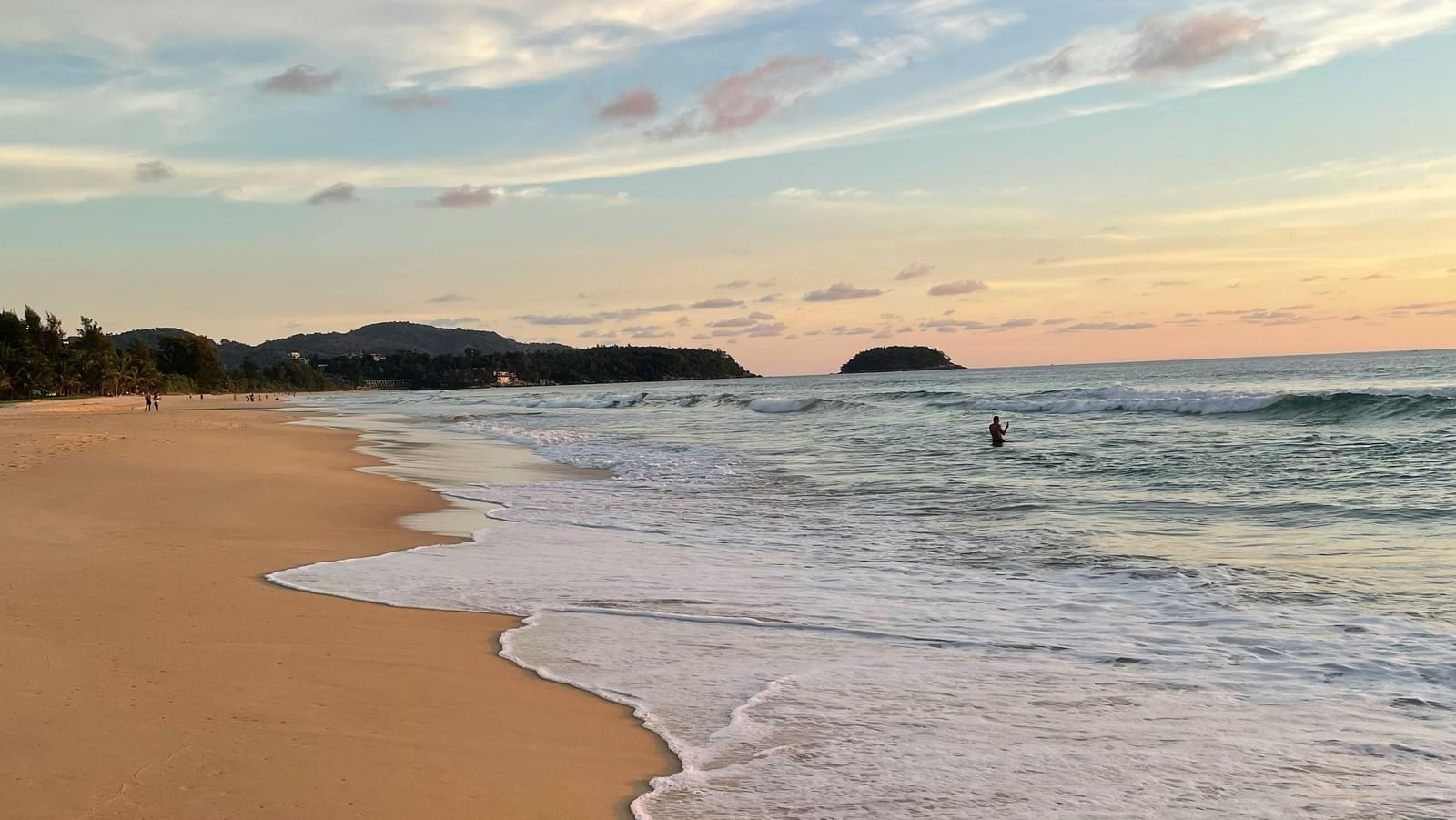 A beach scene at sunset with gentle waves washing onto the sandy shore.
