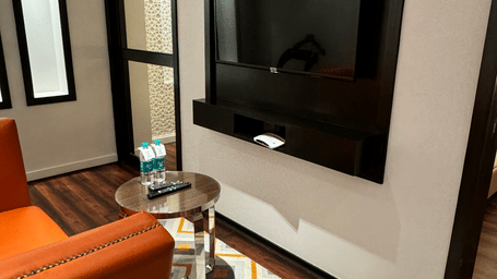A room with an armchair, a wall-mounted television, and a patterned carpet at Cenneys Gateway - Pride of Salem.