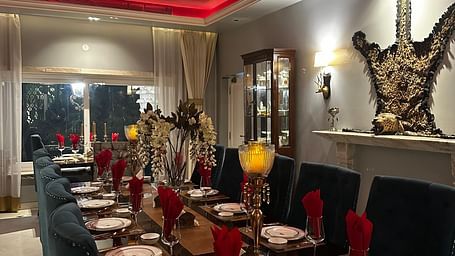 A long dining table set with plates and cutlery, under a red ceiling with neon lighting, in a room with grey walls and decorative wall sconces | Dileep  Kothi, Jaipur