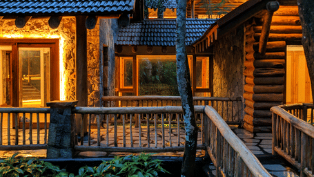 A warm, illuminated wooden villa with a balcony and stone pillars at night, designed by Earthitects.