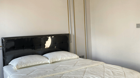 A bedroom featuring a double bed with a black headboard and clean white bedding under soft lighting.