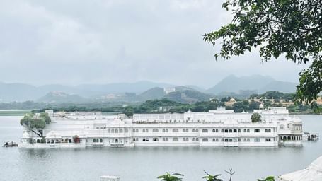 Long view of Jag Mandir under a cloudy sky framed by branches of a tree.