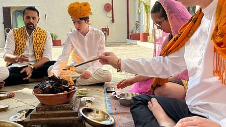 People in traditional attire participate in a ceremony with a fire pit, seated on a patterned rug at Fort Barli, Ajmer.