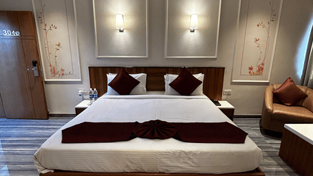 A modern hotel room featuring a double bed, red and white bedding, and two recessed panel lights at Pravasa Hotel, Kolhapur.