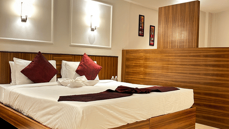 A contemporary double bedroom with a wooden headboard, red throw pillows, and a partial wooden room divider at Pravasa Hotel, Kolhapur.