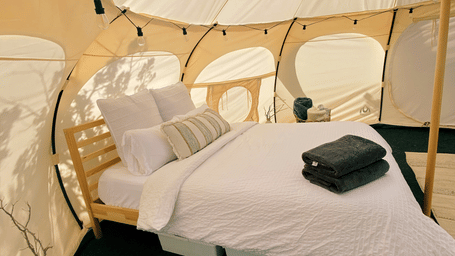 The interior of a modern glamping tent with a bed, chairs, and a window in the ceiling to view the sky.