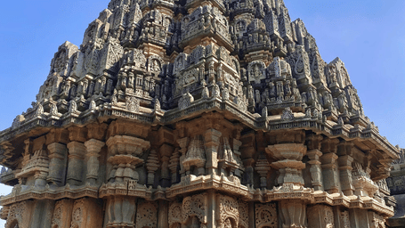 A close-up of an ornate historic Indian temple spire with intricate stone carvings under a clear blue sky.