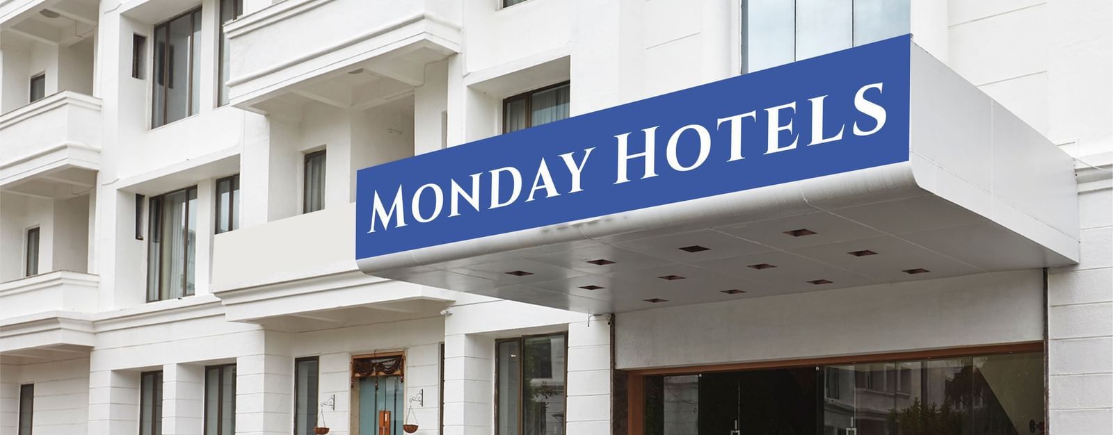 The exterior of a hotel building featuring a huge board on the top of the entrance reading 'Monday Hotels' along with a drive way in front of the building.