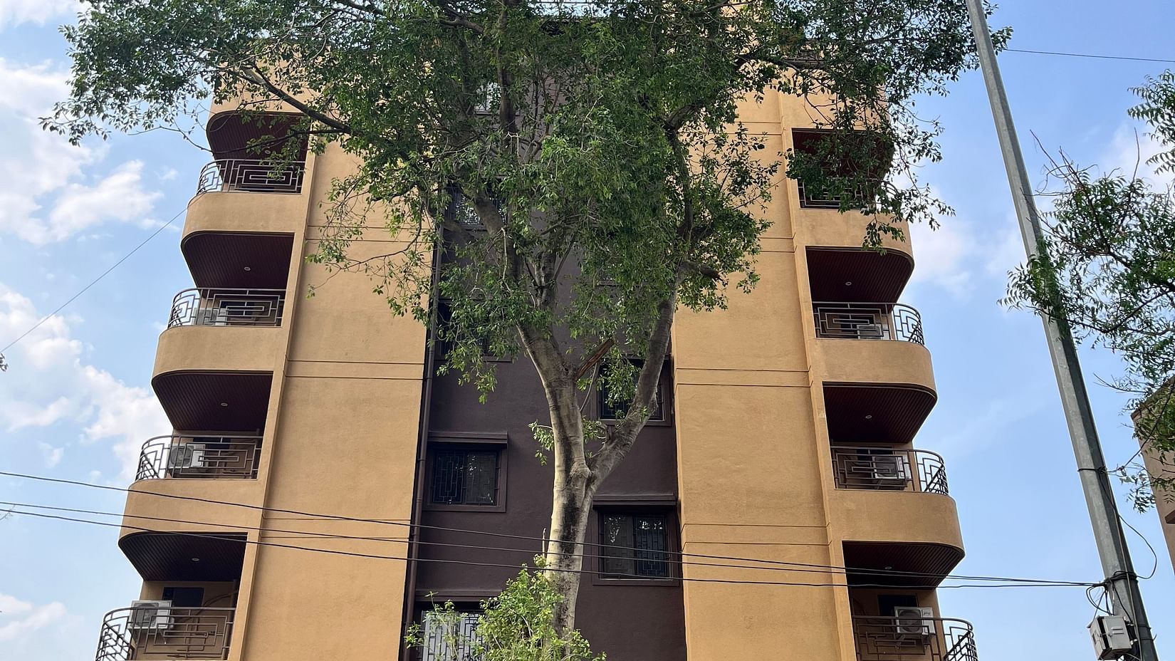 A front view of the hotel with a large tree in front and a sky in background at VITS Select Kharadi, Pune.