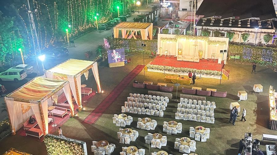 An elevated night view of a large outdoor event setup at Amer Greens, featuring white-clothed round tables, a main stage, and draped canopies.