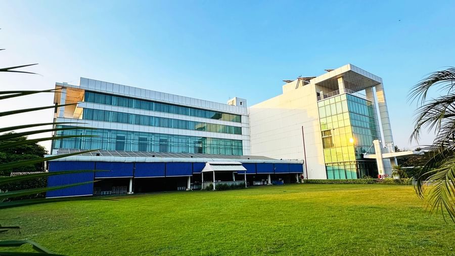  An exterior, wide-angle view of the modern Amer Greens hotel building, featuring multiple stories and a large, manicured green lawn in the foreground under a clear sky.
