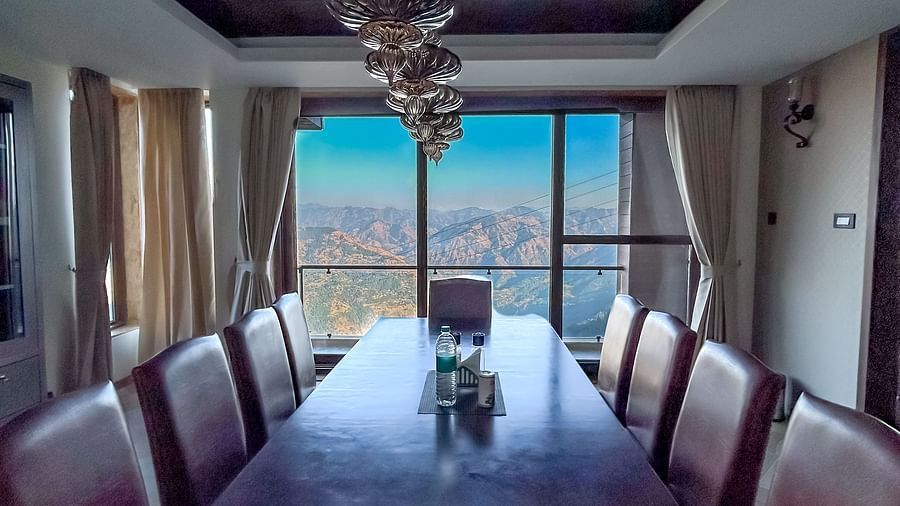 Luxurious indoor dining area with chandelier and full glass view of the mountains at Aranya Himalayan Retreat.