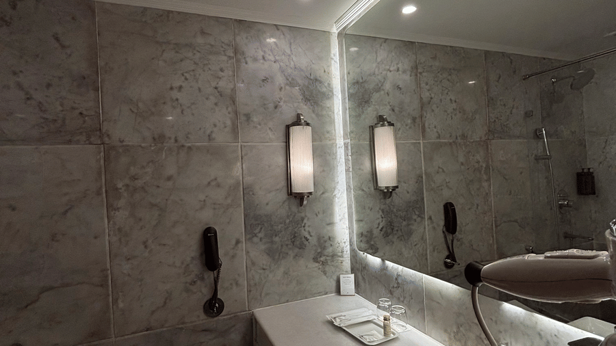 A toilet and vanity area with a wide mirror and integrated lighting occupy the stone-tiled bathroom of the Deluxe Twin at Clarks Amer, Jaipur.