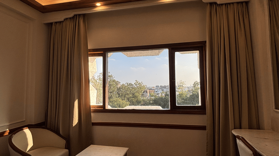A seating area with an armchair and table sits beside a window overlooking the city in the Deluxe Twin room at Clarks Amer, Jaipur.