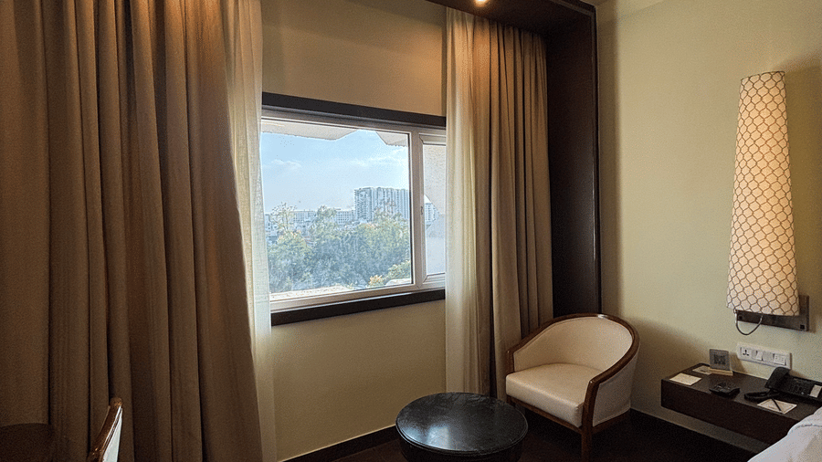 Heavy drapes flank a window and a small seating area with a round table in the Deluxe Twin room at Clarks Amer, Jaipur.
