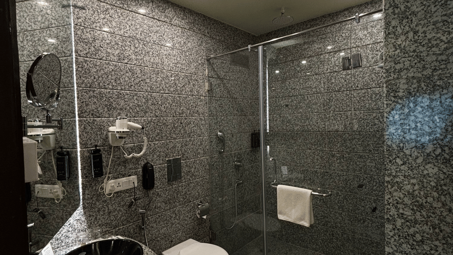 A bathroom in the Superior Twin suite at Clarks Amer, Jaipur featuring a vessel sink, a toilet, and a glass-enclosed shower with stone tiling.