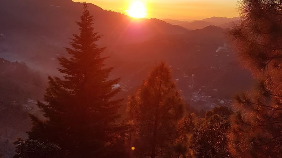 A breathtaking sunset paints the sky with vibrant hues as it dips below the horizon, casting a golden glow over the forested mountain peaks in the distance
