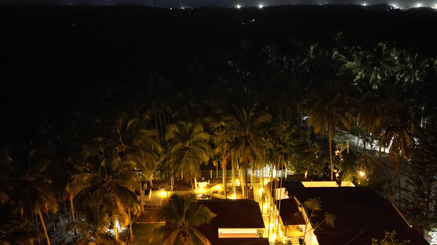 Aerial view of a resort at dusk with illuminated buildings and palm trees, set against a backdrop of mountains.
