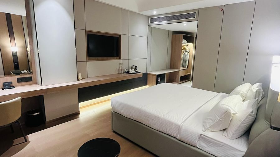 A contemporary hotel room features a king-sized bed, a wall-mounted TV, a desk area, and an orange armchair, with a view towards the bathroom - The Orchid Hotel, Chandigarh