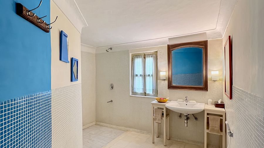 A partial view into a bathroom with a toilet, sinks with mirrors, and a window at Tijara Fort-Palace - 19th Century, Alwar.