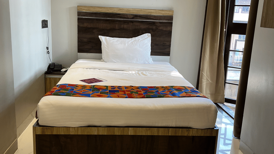 A front view of a bed with a headboard, pillows, side table with a telephone and the entrance to the balcony next to the bed inside Classic Single Room - one of the best hotel rooms in Pune, at VITS Select Kharadi, Pune.