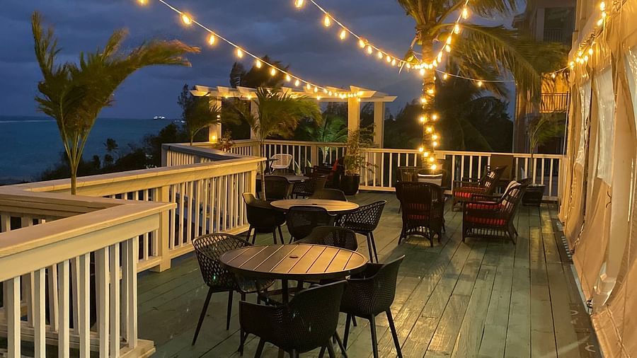 Outdoor dining area with string lights at dusk, white railing and palm trees in view | A Stone's Throw Away