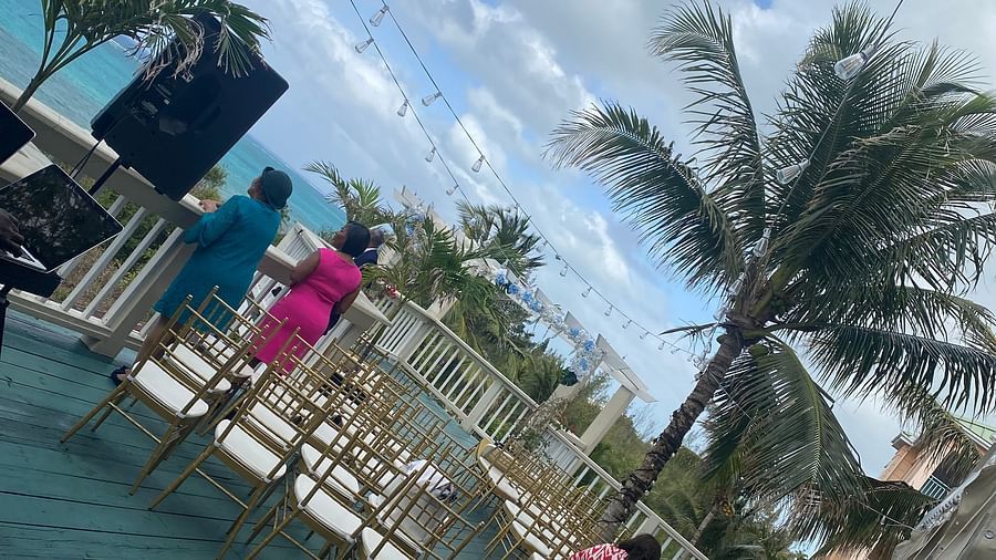 Guests seated on a wooden deck overlooking the ocean with palm trees in the background | A Stone's Throw Away