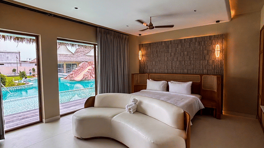 A white curved sofa stands in a bedroom with a view of a blue swimming pool through 2 glass doors at Avanya Resorts N Retreat.