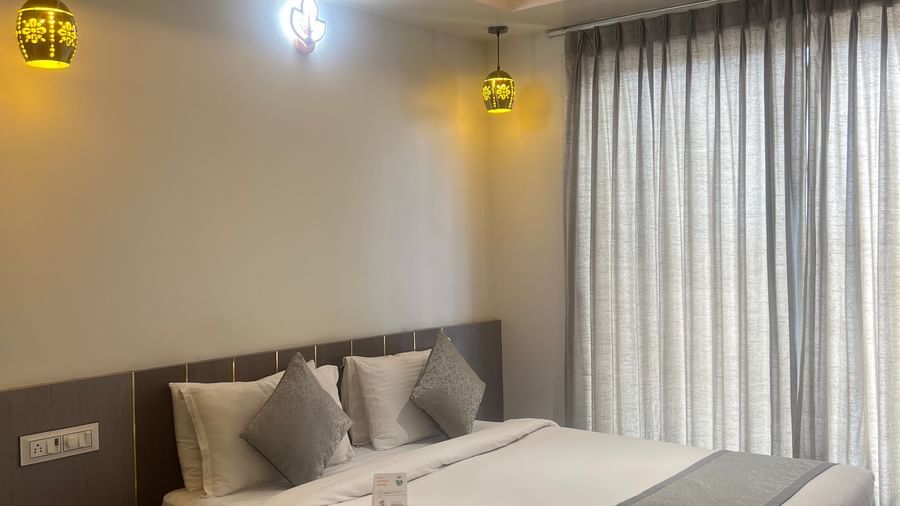 Focus on the double bed in the Daksh Comfort Room at Daksh The Valley Resort, Saputara, seen beside long closed curtains on one side of the room.
