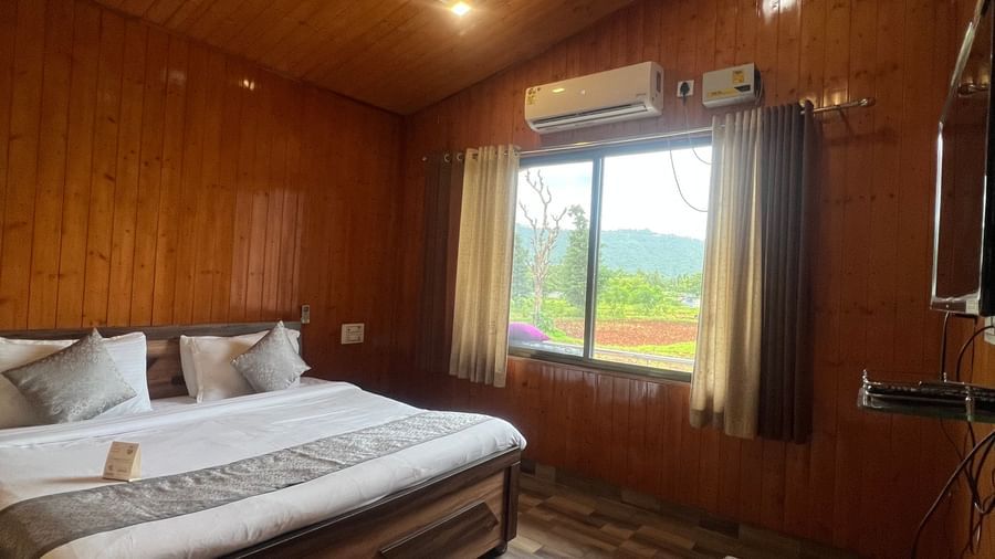Daksh Elite Cottages seen with an A-shaped roof, a window offering views of the surroundings, and a double bed right beside it, at Daksh The Valley Resort, Saputara.