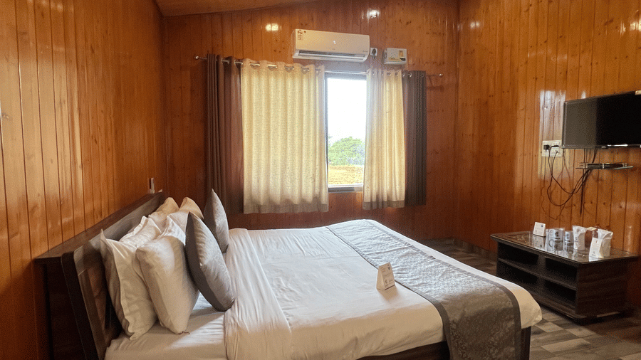 Side view of double bed and a window beside it at Daksh The Valley Resort, Saputara.