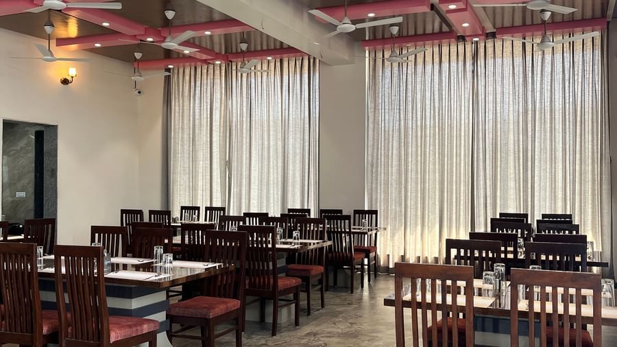 Close up of a row of dining tables neatly arranged in front of long closed curtains at Daksh The Valley Resort, Saputara