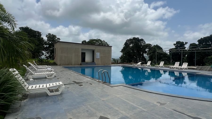 Outdoor swimming pool surrounded by deck and resort grounds at Daksh The Valley Resort, Saputara, with a backdrop of mountains.
